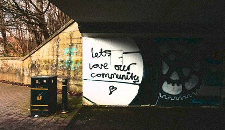 Graffiti on a wall under a bridge reads 'lets love our community'